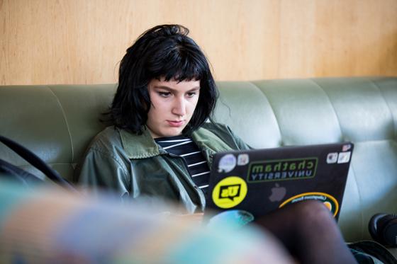 Photo of a female Chatham University student sitting on a couch in the library, working on her laptop